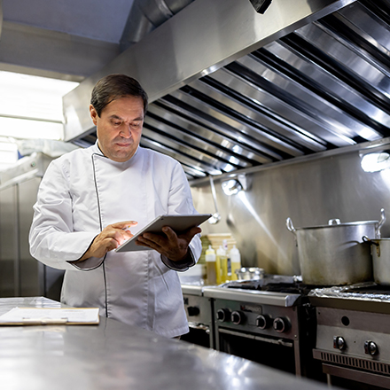 Chef cuisinier dans sa cuisine tenant une tablette dans ses mains